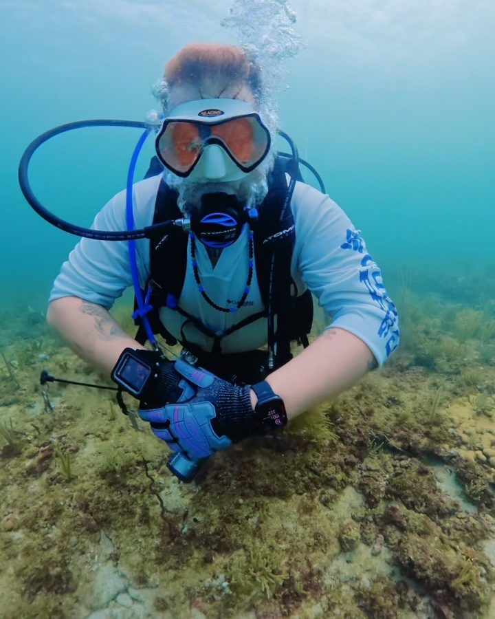 Ben underwater in full scuba gear, kneeling on the sand